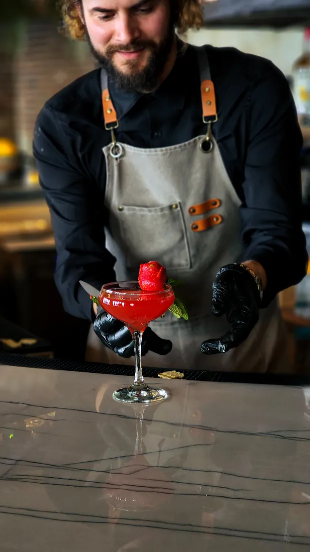 A bartender presenting a red cocktail